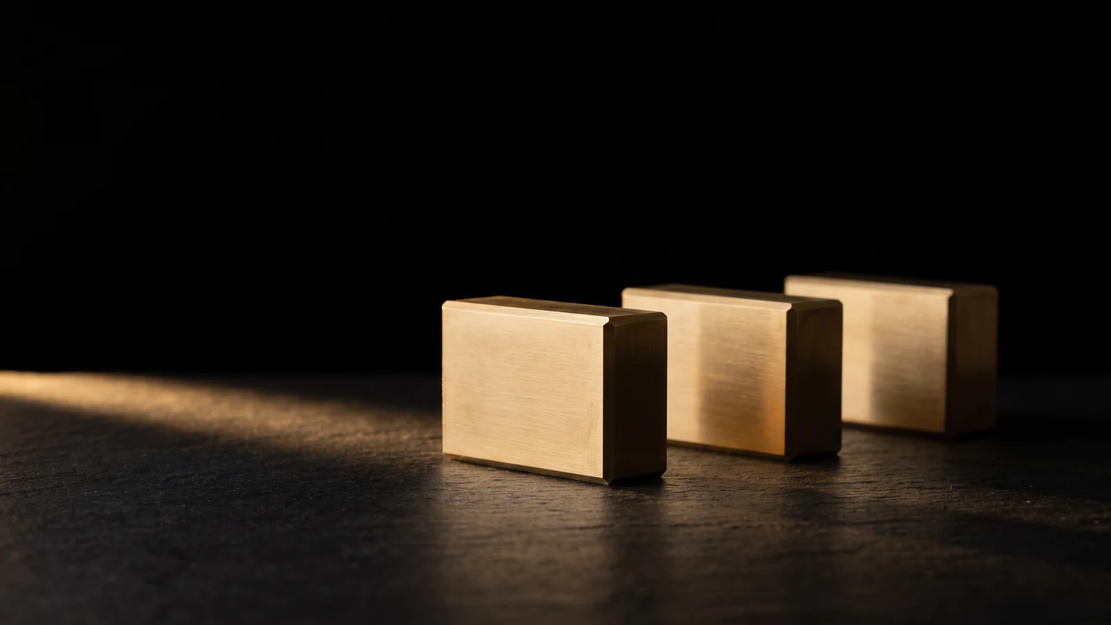 Three identical brass blocks of the same height standing in a row on black stone.