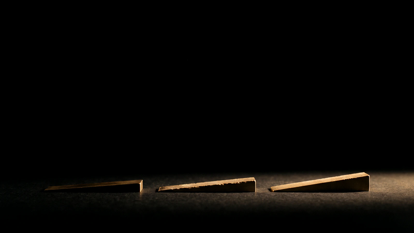 Three small brass wedges low in the frame on black, rising slightly from left to right.